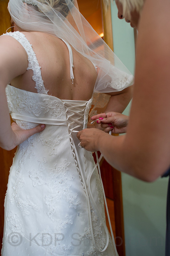 A bridesmaid lacing the back of a wedding gown before the ceremony